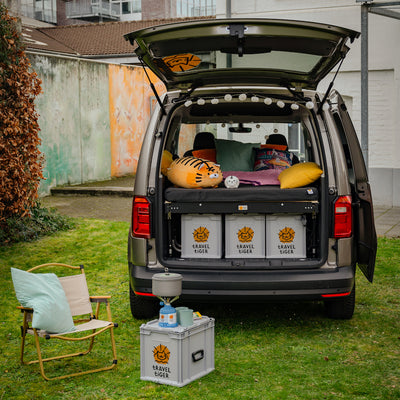 VW Caddy stands in the garden with open trunk and camping bed.