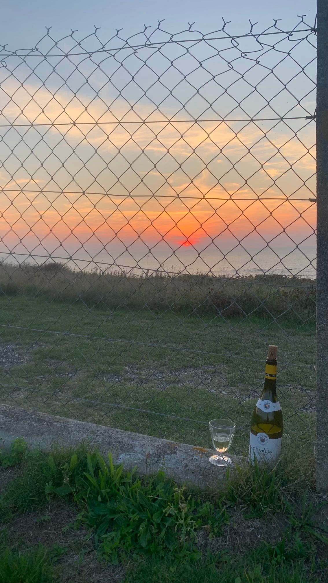 Weinflasche und Weinglas stehen auf dem Boden - im Hintergrund der Sonnenuntergang