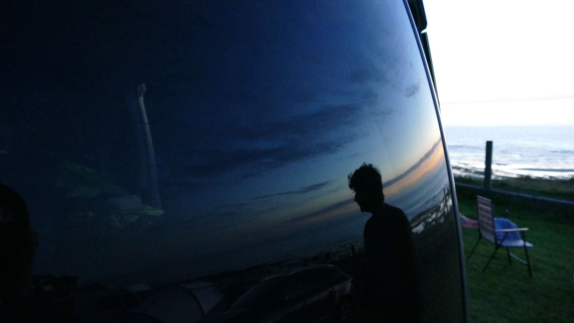 Mann spiegelt ist im Autofenster - im Hintergrund der Sonnenuntergang