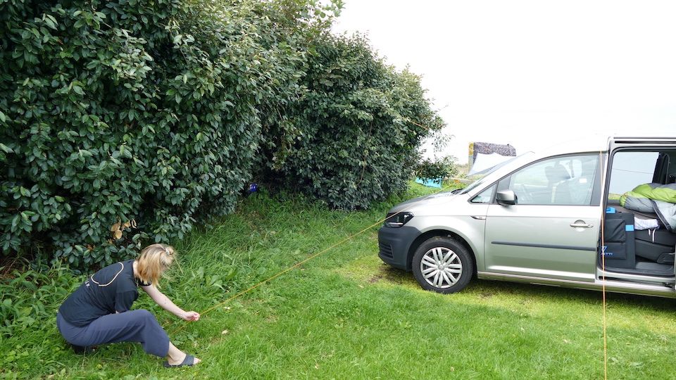 Frau baut Sonnensegel beim Auto Camping auf uns spannt es über das Autodach.
