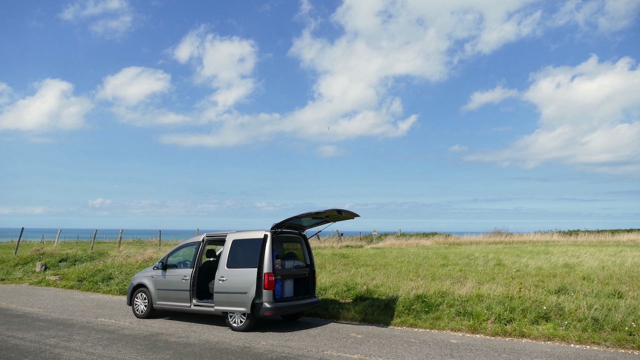VW Caddy steht am Feldrand mit Meer im Hintergrund.