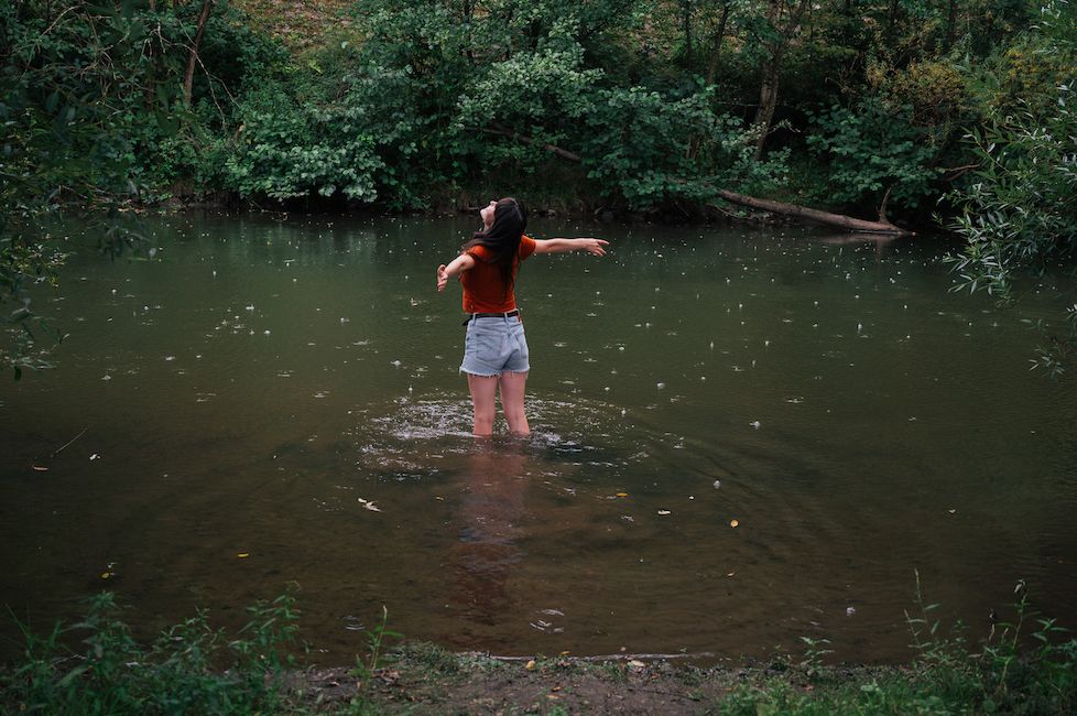 Junge Frau steht in einem Fluss und genießt einen kleinen Sommerregenschauer.