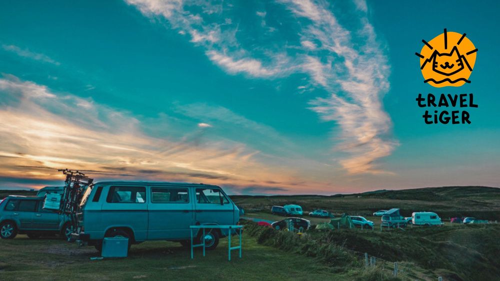 Einige Campingfahrzeuge stehen in einer leicht hügeligen Landschaft verteilt, während am Himmel die Sonne untergeht.