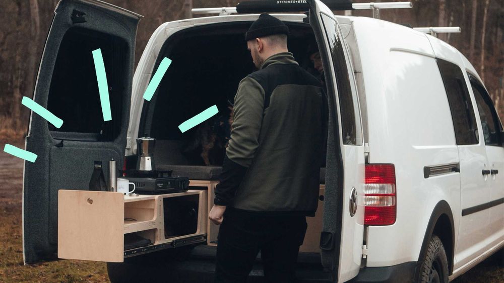 Mann steht an einer ausziehbaren Campingküche im Kofferraum eines VW Caddys.
