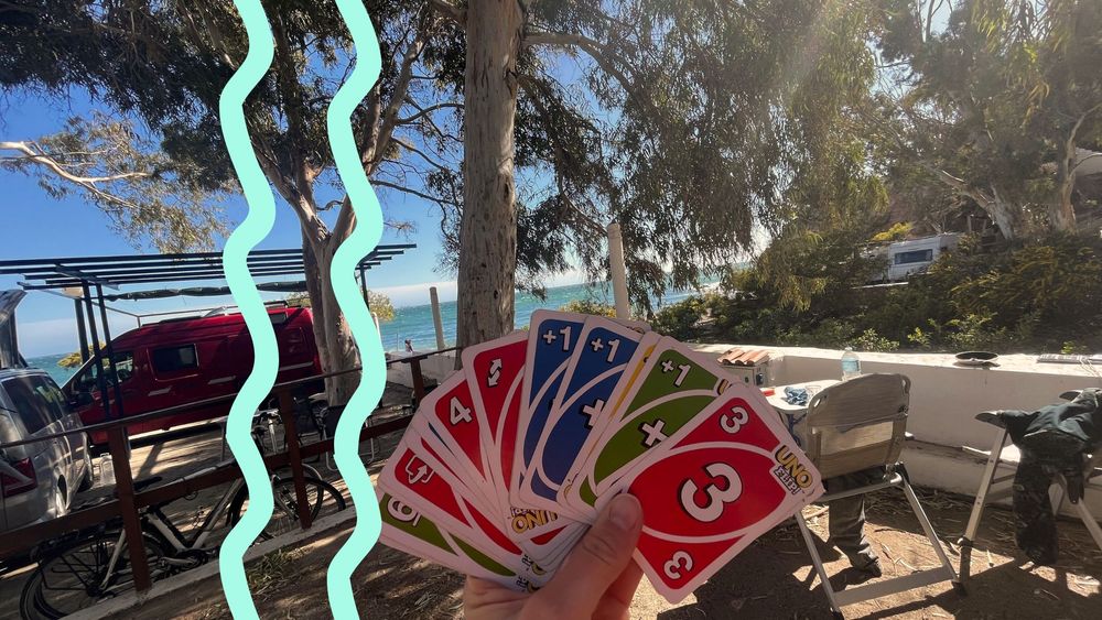 Eine Hand voll mit Unokarten vor einem Campingstellplatz mit Meerblick.
