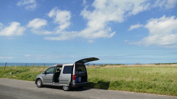 VW Caddy steht am Feldrand mit Meer im Hintergrund.