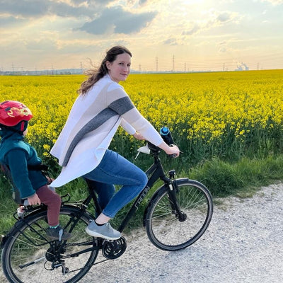 Profilfoto von Lena mit Kind auf dem Fahrradgepäckträger auf einem offenen Feld.