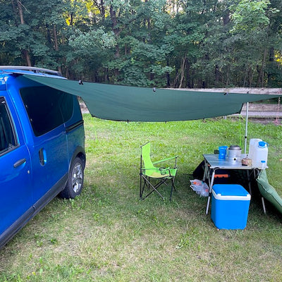 A mini camper with an awning stands on a meadow.