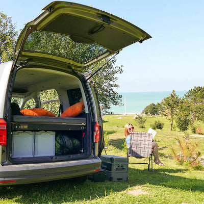 Anna sitzt neben dem Caddy im Campingstuhl und liest.