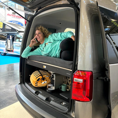 Employee Maike is lying on the camping bed in the VW Caddy and talking on the phone.
